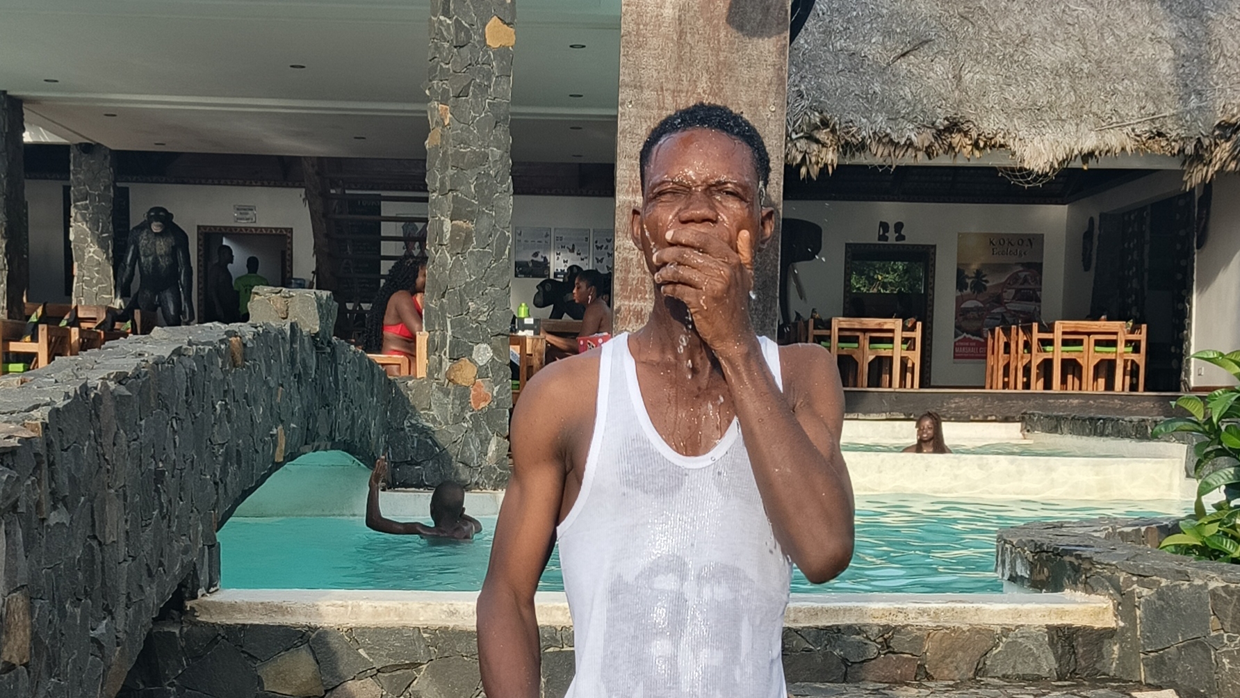 Nathan R. Watalah standing poolside at tropical resort during semester break in Liberia, resort restaurant in background